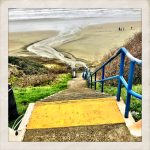 Color photograph of verticle stairs leading down to a beach that opens to the ocean in Lincoln City, Oregon.