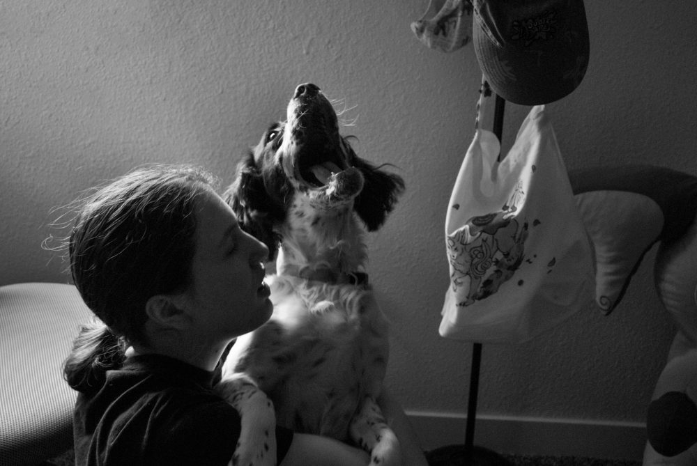 The photo is of a girl holding a dog that is looking up with an open mouth. The photo is in black and white.