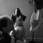The photo is of a girl holding a dog that is looking up with an open mouth. The photo is in black and white.