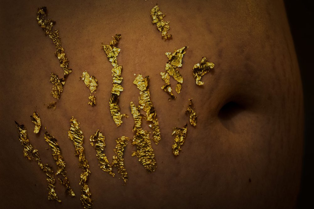 Macro photo of a stomach taken from the side, stretch marks are covered in gold leaf flakes.