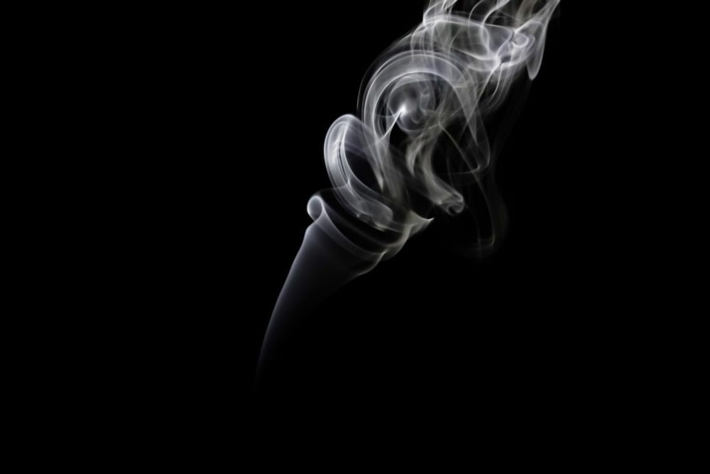 A photograph of smoke coming from an incense holder, captured by wind movement, flashlights, and backdrops.
