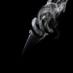 A photograph of smoke coming from an incense holder, captured by wind movement, flashlights, and backdrops.