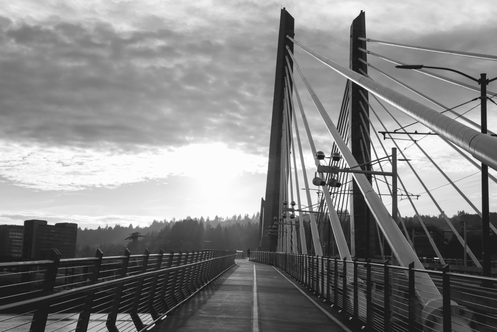 A black and white photo of the path on Tilikum Crossing with a background of clouds and trees.