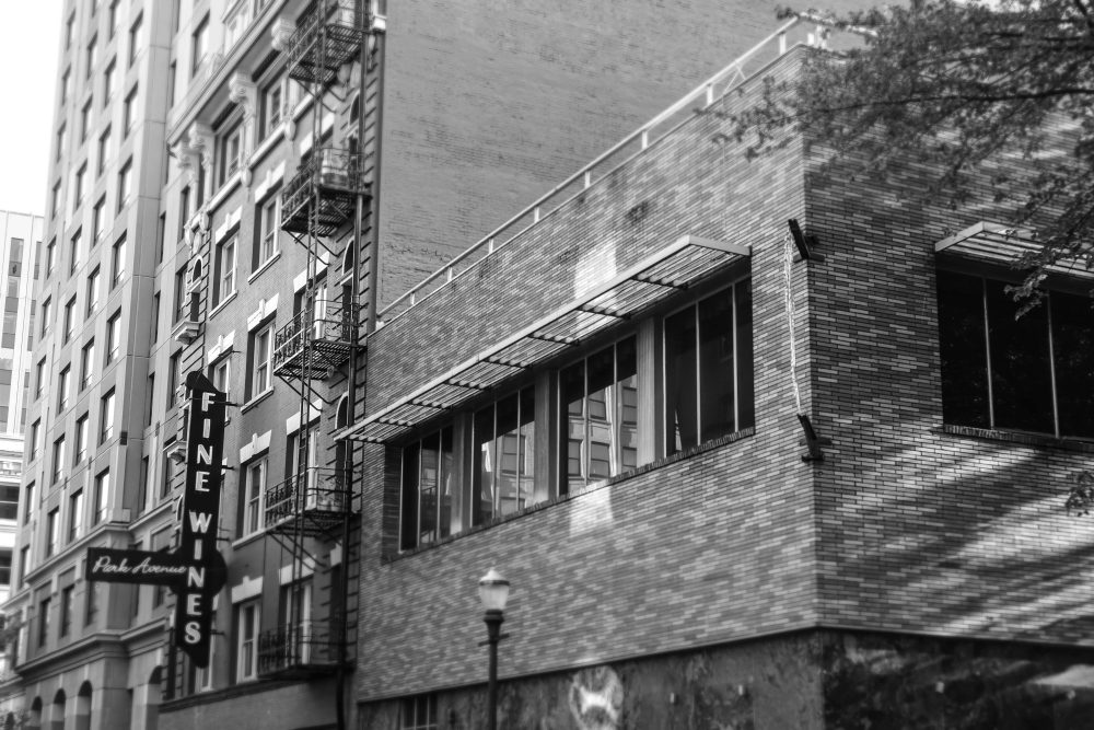 A black and white photo of a vertical sign with the words "Fine Wines" written on it, with the sign attached to a building in the city.