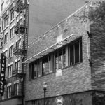 A black and white photo of a vertical sign with the words "Fine Wines" written on it, with the sign attached to a building in the city.