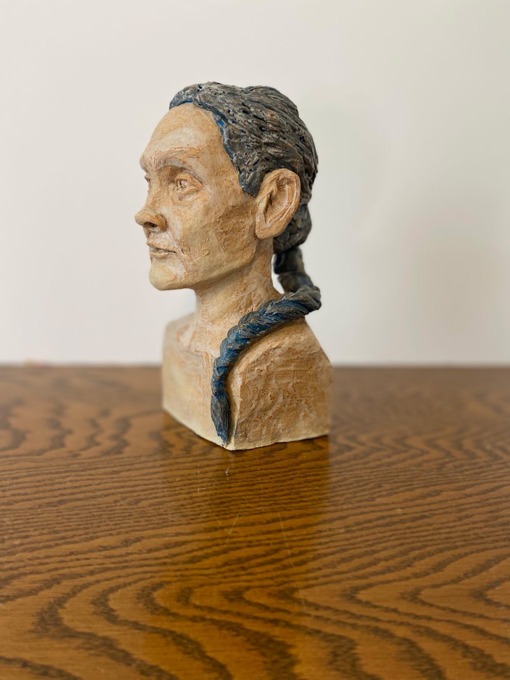 Ceramic representation of a middle aged person with a blank gaze and a blue braid.