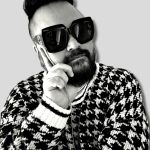 A black and white photo of a man in fashionable attire in a thinking pose.