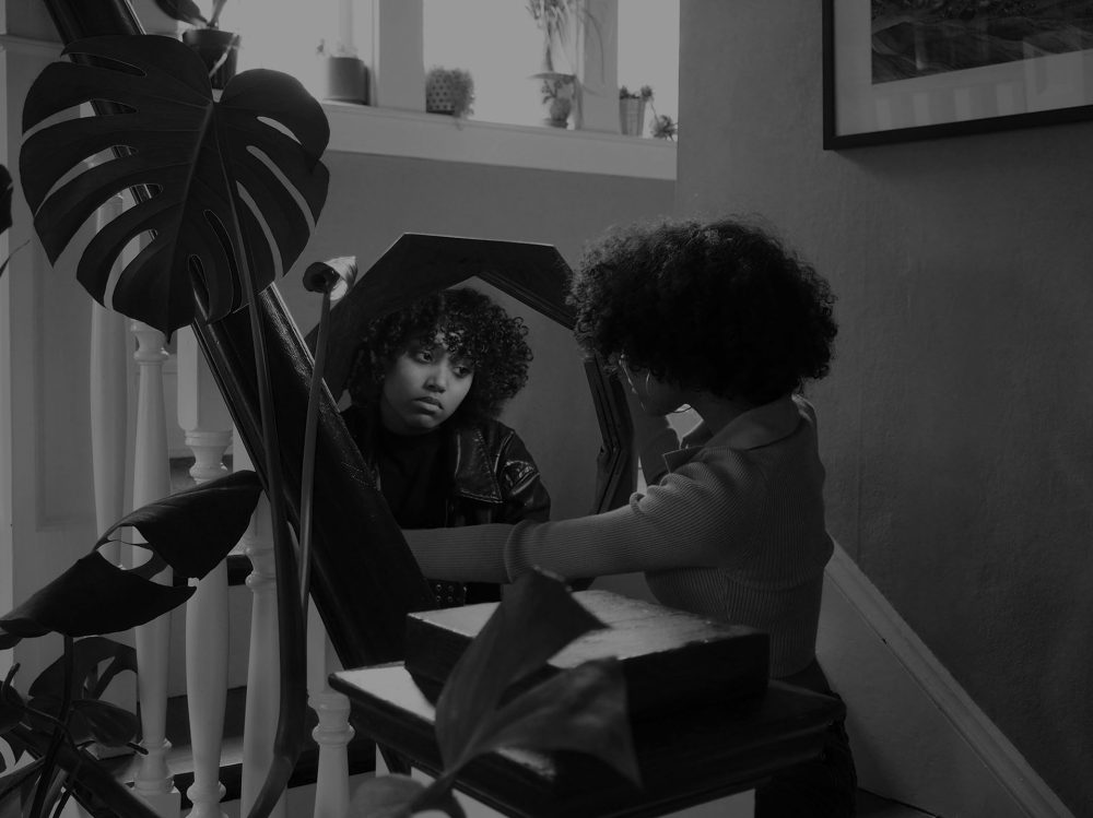 A black and white photo of a person staring into their reflection.