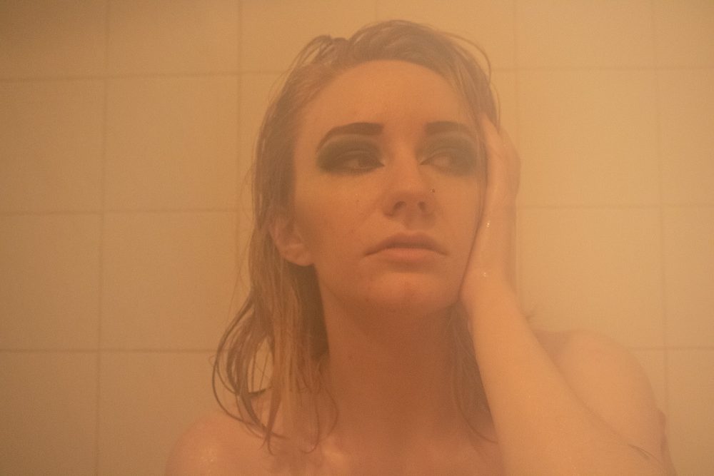 A young woman sits in a tub with her head in one hand while looking to the side.