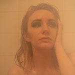 A young woman sits in a tub with her head in one hand while looking to the side.