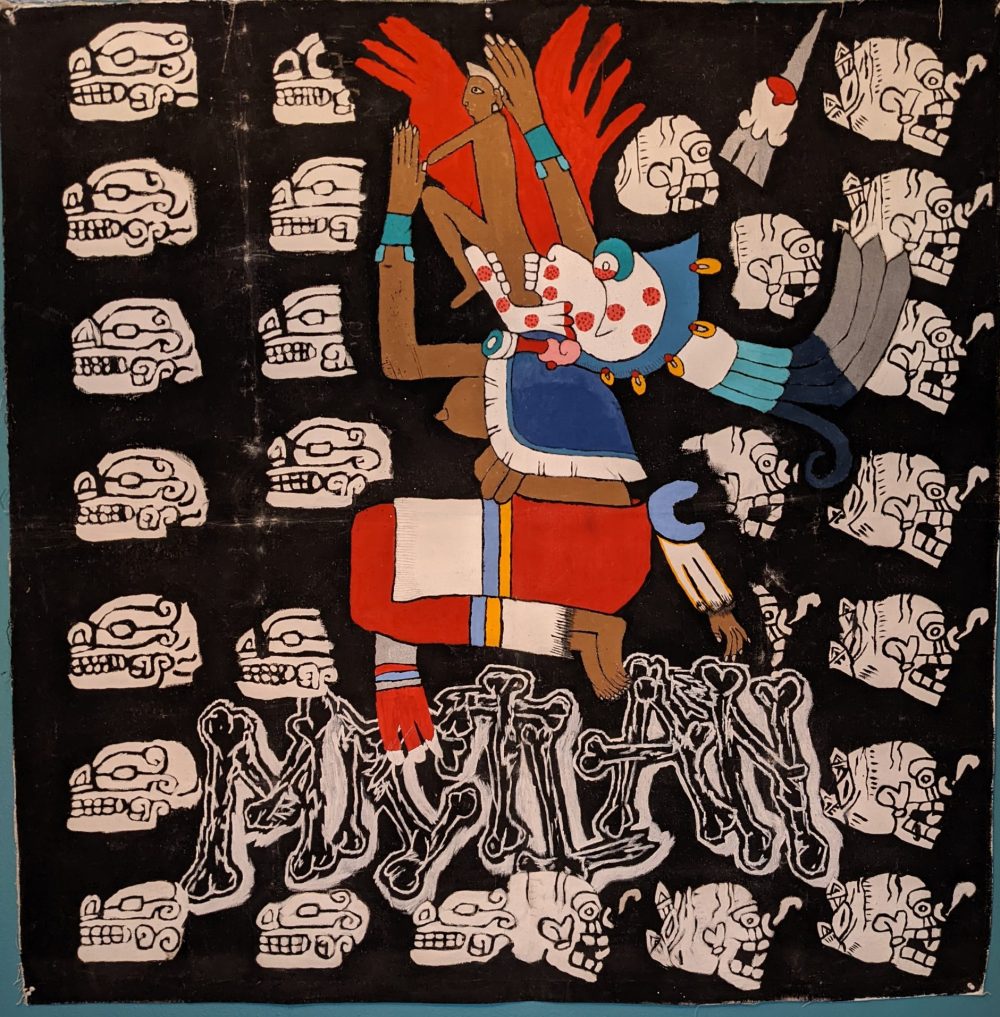 A painting depicting the Goddess Mictecacihuatl, coming out of her mouth is a representation of rebirth in the form of a small humanoid; surrounding her are white skulls on a black background and beneath her is the word "Mictlan" in bone lettering which is the indigenous name for the underworld.