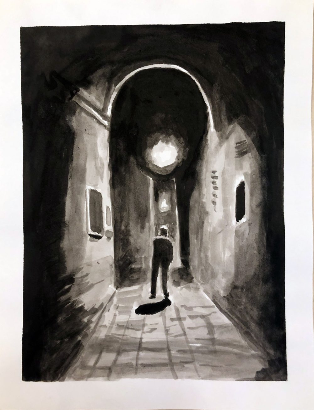 Man walking in light down a dark street.