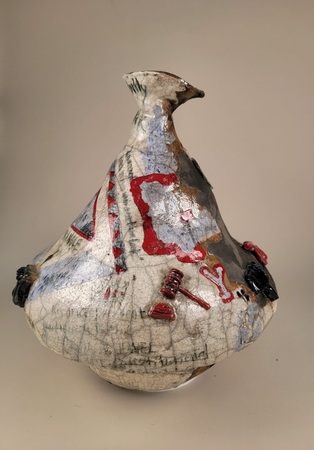 A large, off-centered and wonky pot, decorated with 2D slip and glaze designs in light blue, red, and black, and 3D medallions sculpted into various shapes, glazed, and attached to the surface of the pot.