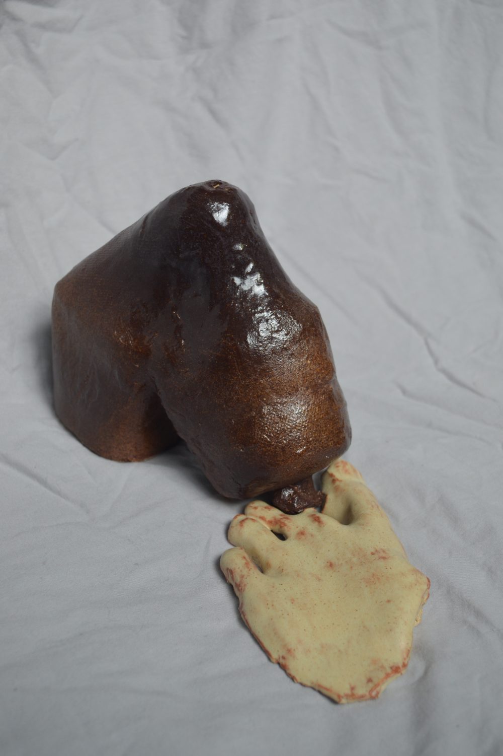 A sculpture of a burgundy water bottle that is bent down, facing the ground, being opened by part of a beige foot.