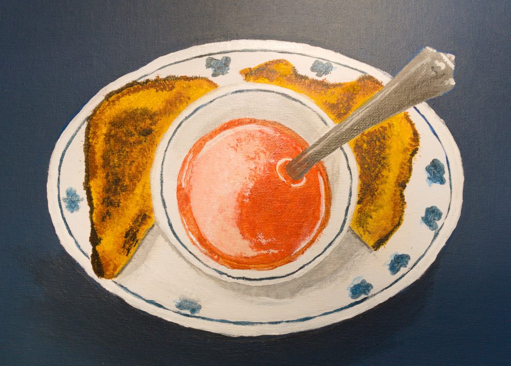 An oval plate with blue flowers holding two halves of toasted bread and a small white bowl of red-orange tomato soup, with the silver handle of a spoon sticking out of it.