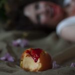 A bloody bitten apple in focus in the foreground and a person smiling in the background out of focus.