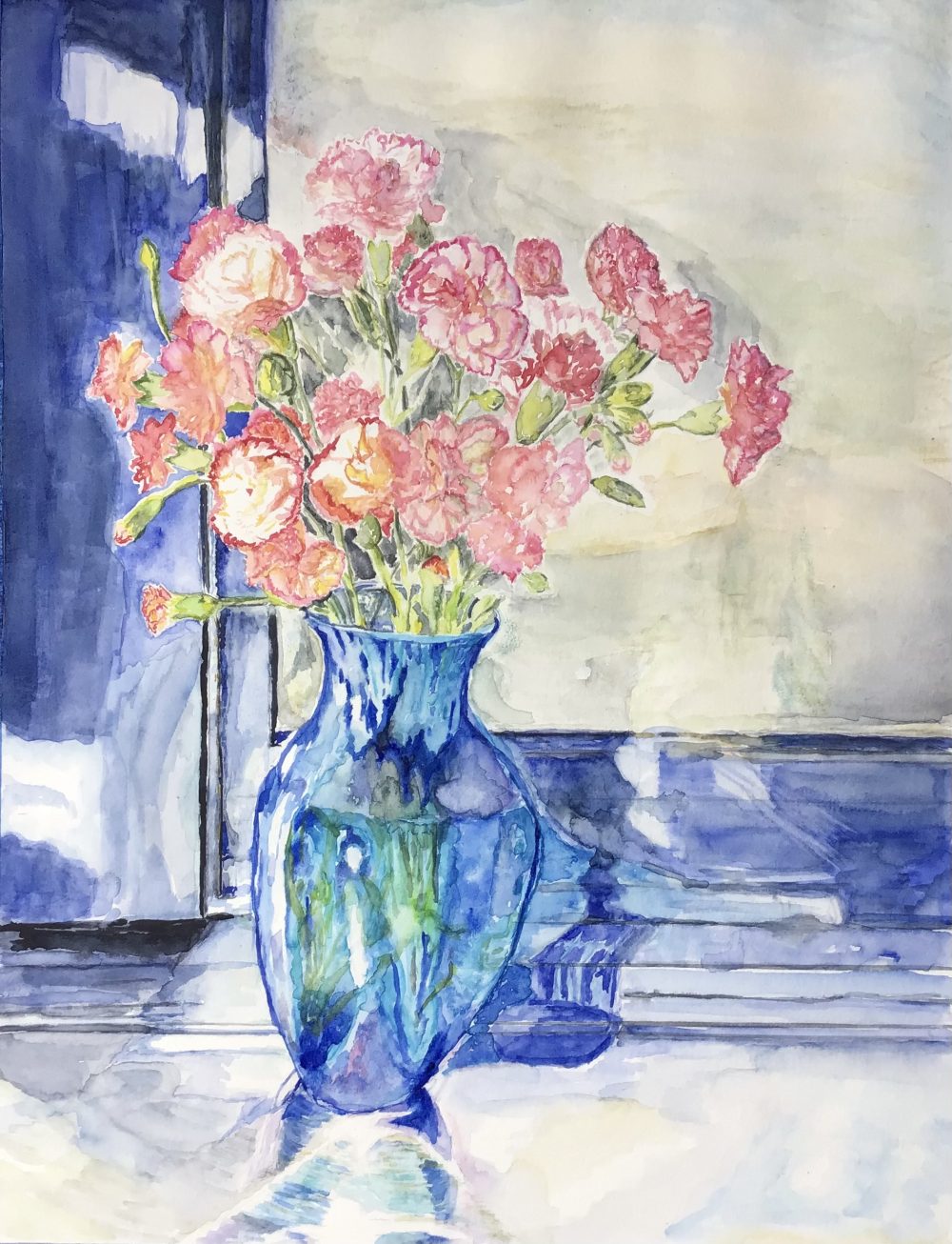Mid-morning sunlight is striking the front of a blue glass vase with bunch of orange-pink carnations on a stainless steel counter set in front of a window with an indigo frame.