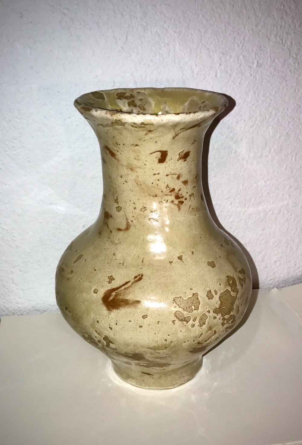 A tan, marbled vase that is wider towards the bottom, narrows at the neck, and flares at the top.