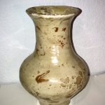 A tan, marbled vase that is wider towards the bottom, narrows at the neck, and flares at the top.