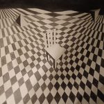 Black and white drawing of a chair in the middle of this squared space, while the geometrical triangles and diamonds flow sacredly around the chair