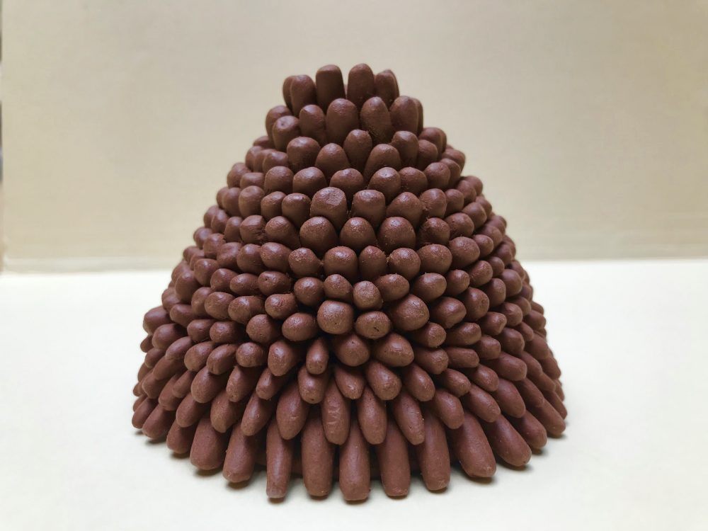 A cone shaped ceramic sculpture, wider at the base and tapering to the top, small brown coils stacked in layers like a pyramid