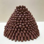 A cone shaped ceramic sculpture, wider at the base and tapering to the top, small brown coils stacked in layers like a pyramid