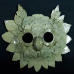A ceramic mask with a sage green glazed, made of many clay leaves to look like an owl.