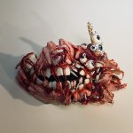 A 3D sculpture of a mask that looks like torn flesh and muscle over the jaw and teeth bones - some bones showing through the flesh with several eyes and broken bones sticking out on a white background.