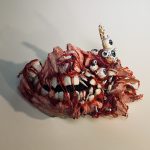 A 3D sculpture of a mask that looks like torn flesh and muscle over the jaw and teeth bones - some bones showing through the flesh with several eyes and broken bones sticking out on a white background.