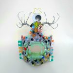 A sculpture of a glittery white monster mask, covered with an assortment of plastic and metal embellishments.