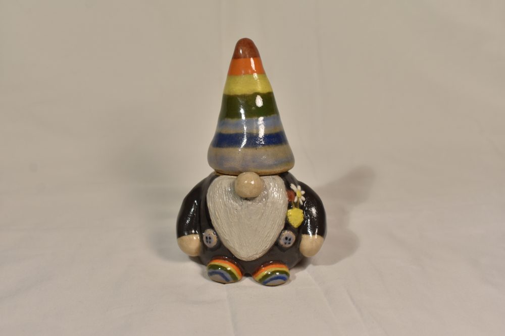 A ceramic statue of a gnome, painted dark grey with purple suspenders and rainbow hat and shoes.