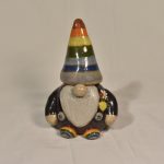 A ceramic statue of a gnome, painted dark grey with purple suspenders and rainbow hat and shoes.