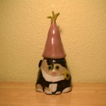 A small ceramic container shaped as a grey, beige and white cat with a removable pink hat on to store cat treats in.