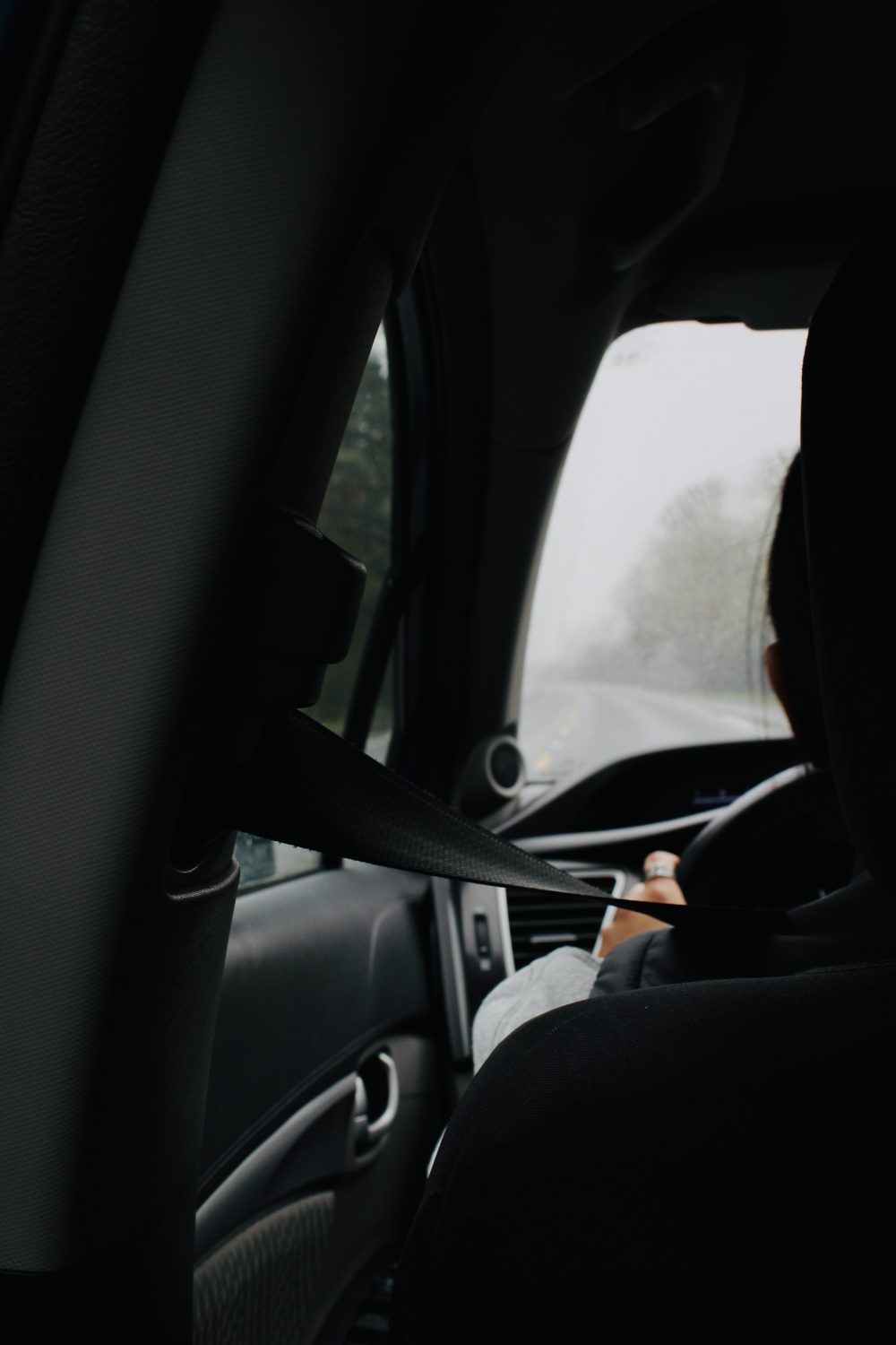 A photograph taken from the back seat of a car looking over the driver's shoulder and out the front window.