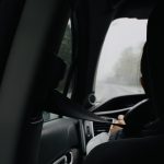 A photograph taken from the back seat of a car looking over the driver's shoulder and out the front window.