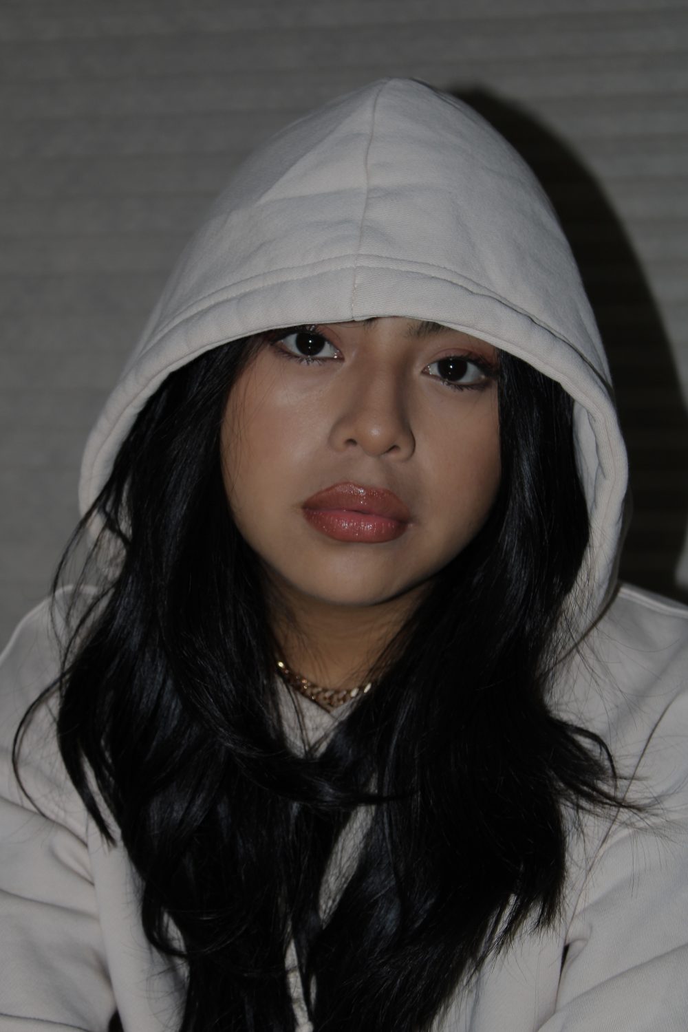 A photograph of a young woman wearing a white hoodie sweatshirt with long black hair.