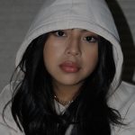 A photograph of a young woman wearing a white hoodie sweatshirt with long black hair.