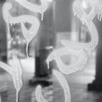 A photo in black and white of indistinct graffiti spray painted across the windows of a government building containing tall pillars and a checkered floor.