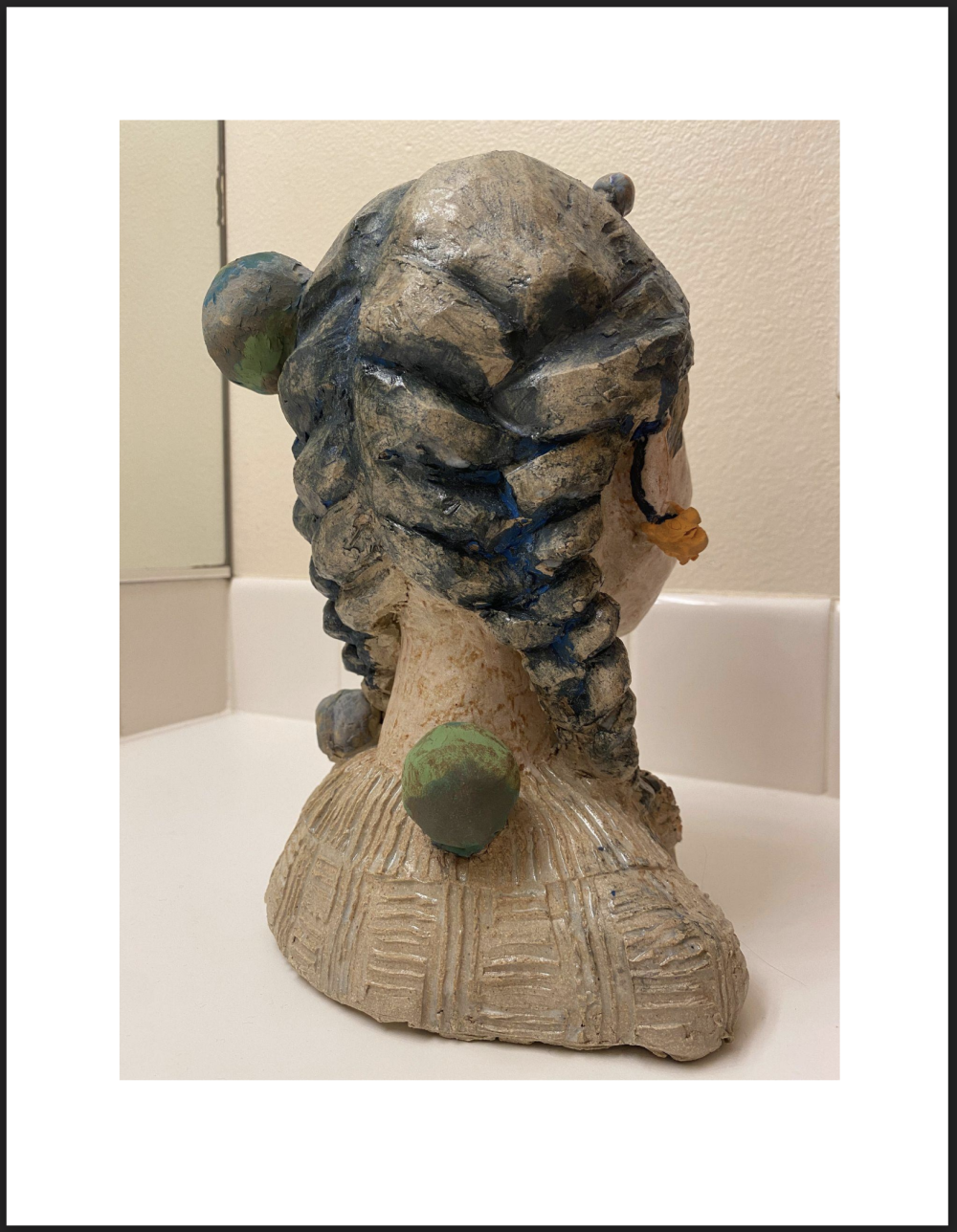 A sculpture of a 19 year old lady's head with blue, yellow and white glaze on it; she is looking up in the air and dreaming of her future, and around her, you can see her lovely cat and small planet sculpted on her.
