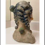 A sculpture of a 19 year old lady's head with blue, yellow and white glaze on it; she is looking up in the air and dreaming of her future, and around her, you can see her lovely cat and small planet sculpted on her.