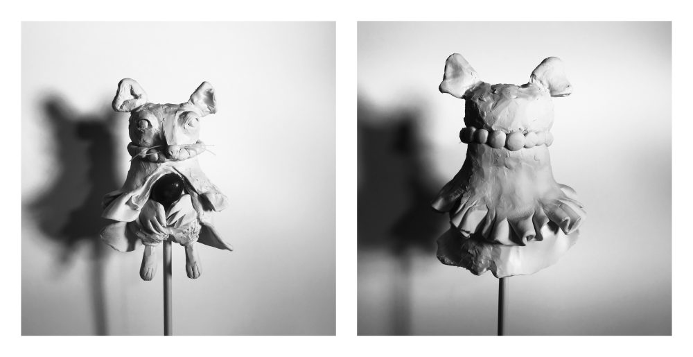 The sculpture looks like a mouse, has whiskers, long feet, trousers, a robe, and beaded necklace. It holds a jasper stone at the center of its belly.