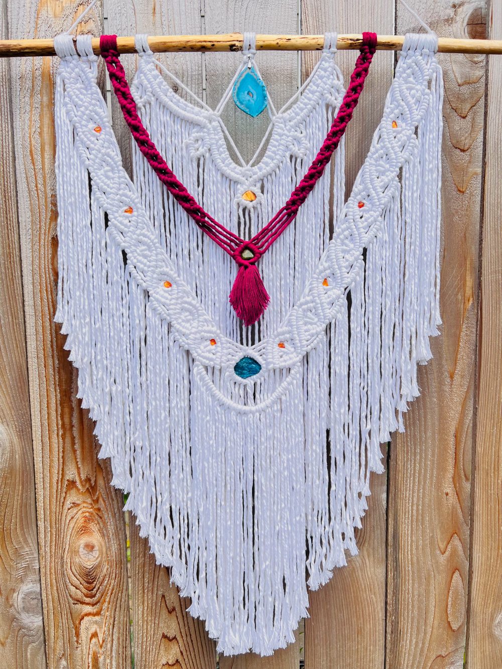 A fiber sculpture of mostly white cotton thread with woven and loose elements, red thread and yellow and blue stone accents.