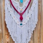 A fiber sculpture of mostly white cotton thread with woven and loose elements, red thread and yellow and blue stone accents.