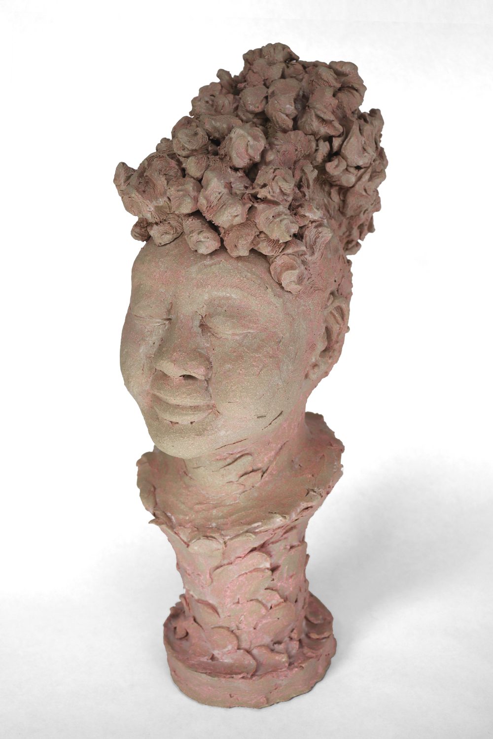 Sculpted portrait of a woman with her eyes closed into a slight smile with round cheeks, hair is pulled back into a poof of curls, details of ear piercings on both ears, the base is built of petal-like smudges pushing up into the collar and neck of the bust as slight pink stains come through in the deeper edges.