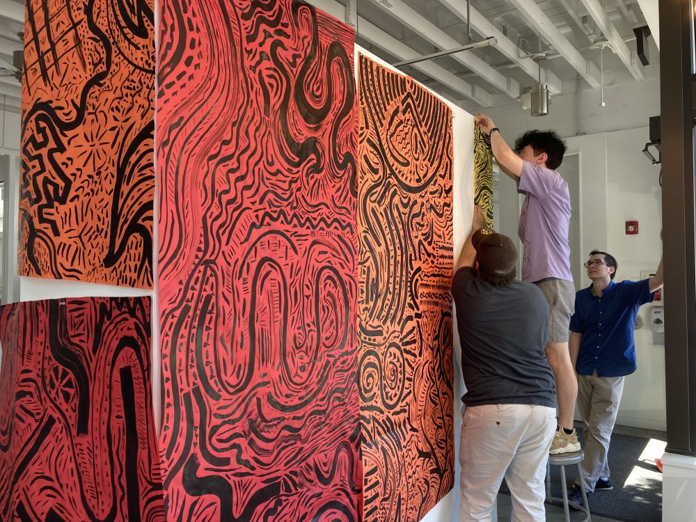 Students hang drawings on the gallery walls.