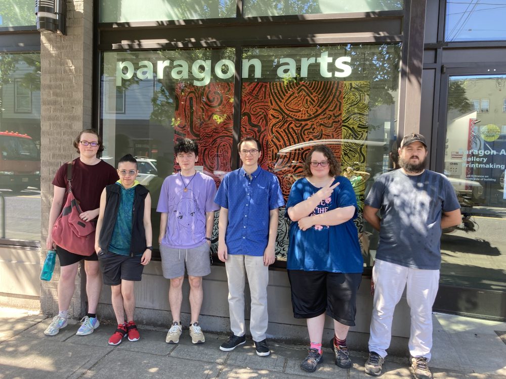 Six students stand in front of the Paragon Arts Gallery windows.