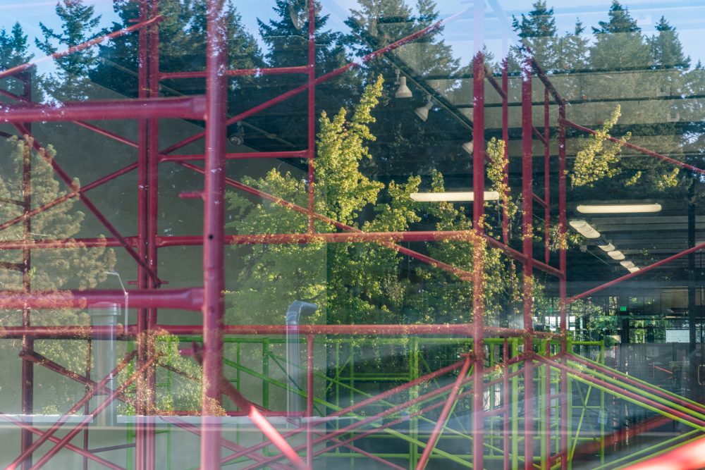 Pink and green scaffolding and trees reflected in the window.