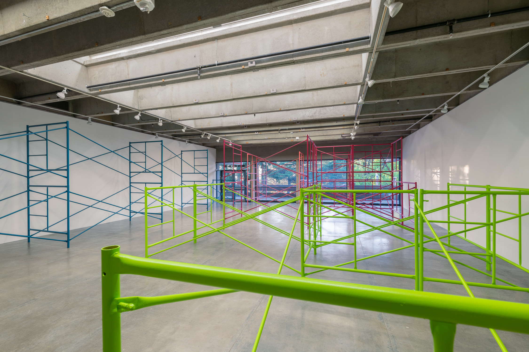 Teal, green, pink scaffolding in a gallery.