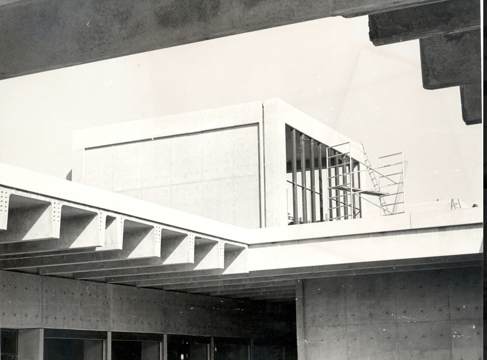 Black and white photograph of a Brutalist building with a scaffold on the roof.
