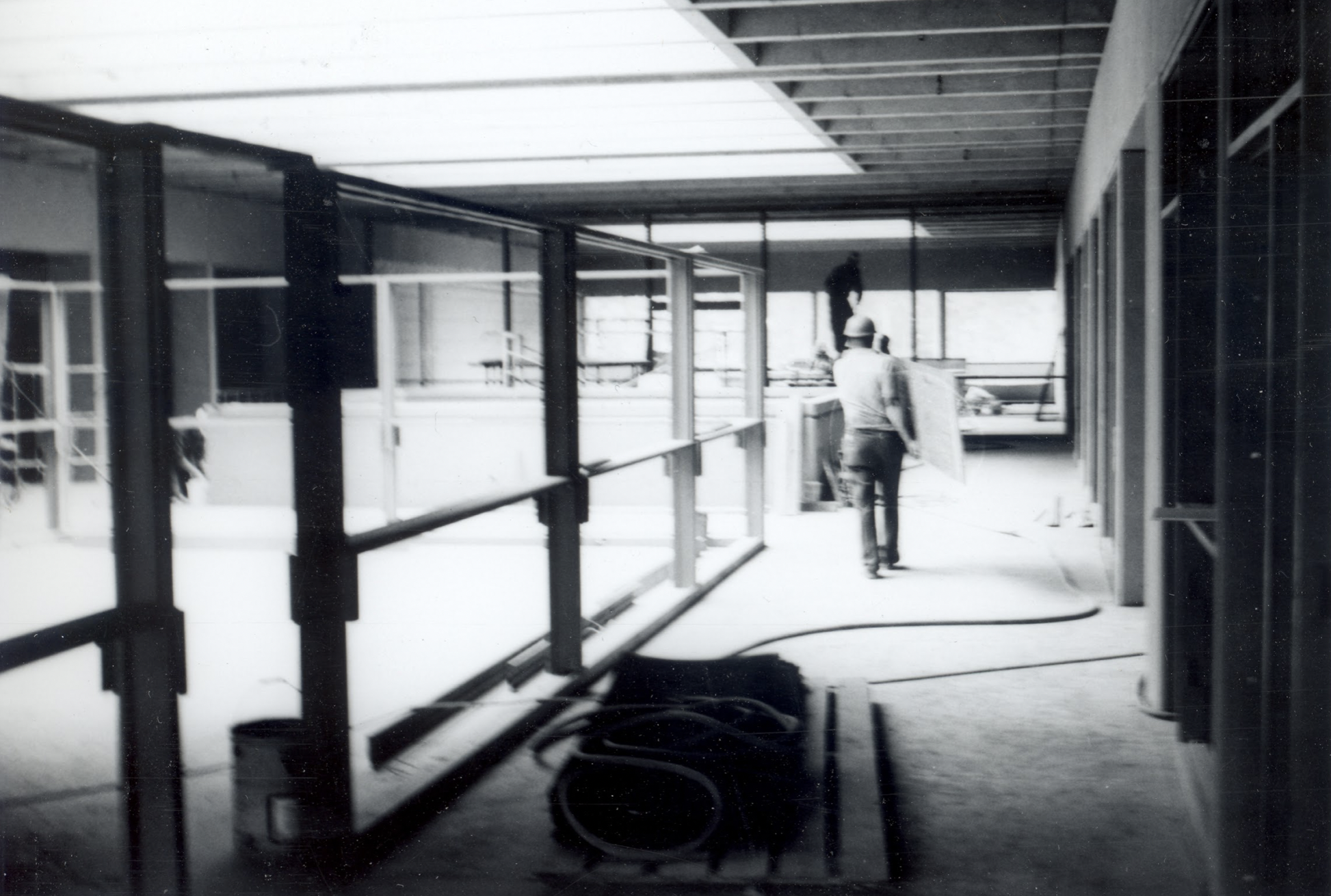 Black and white photograph of workers carrying material in a building under construction.